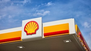 Close-up of the Shell logo displayed on a fuel station canopy against a blue sky with scattered clouds.