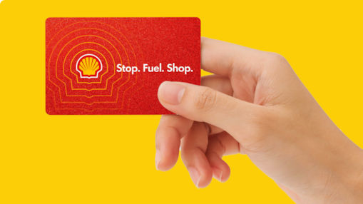 Hand holding a red Shell-branded card featuring the Shell logo and the words “Stop. Fuel. Shop.” against a yellow background.