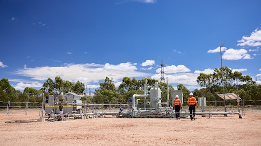 Shell QGC employees walking toward gas well infrastructure in rural Queensland.
