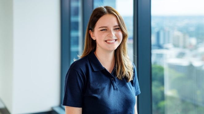 An individual smiling and standing by an office window