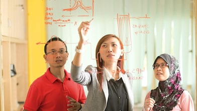 Colleagues gathered standing and discussing metrics on a glass board