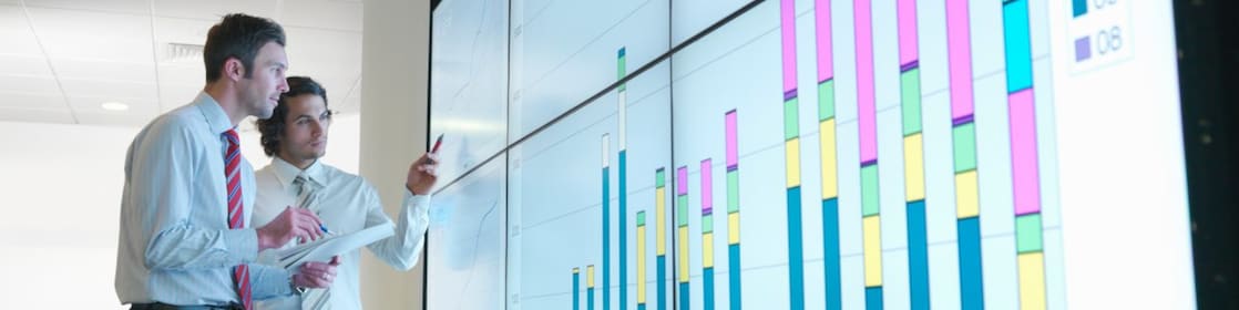 Business men analyse reports displayed on a large digital screen