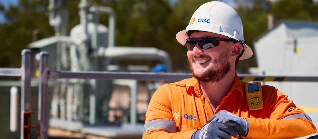 A Shell QGC worker wearing personal protective equipment using a walkie talkie at an outdoor work site in Queensland.