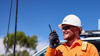 A Shell QGC worker wearing personal protective equipment using a walkie talkie at an outdoor work site in Queensland.