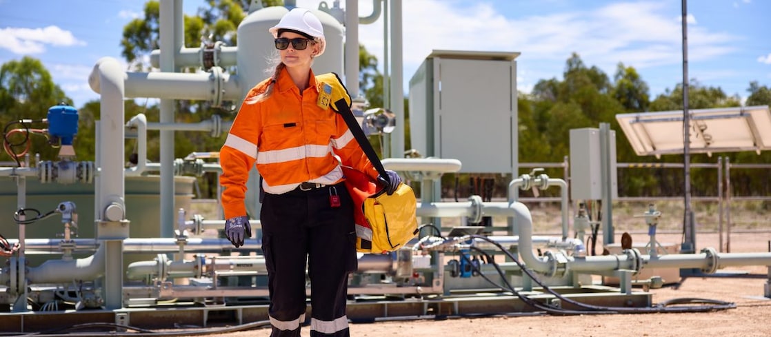 A Shell QGC worker wearing personal protective equipment walking in front of a gas well in Queensland.