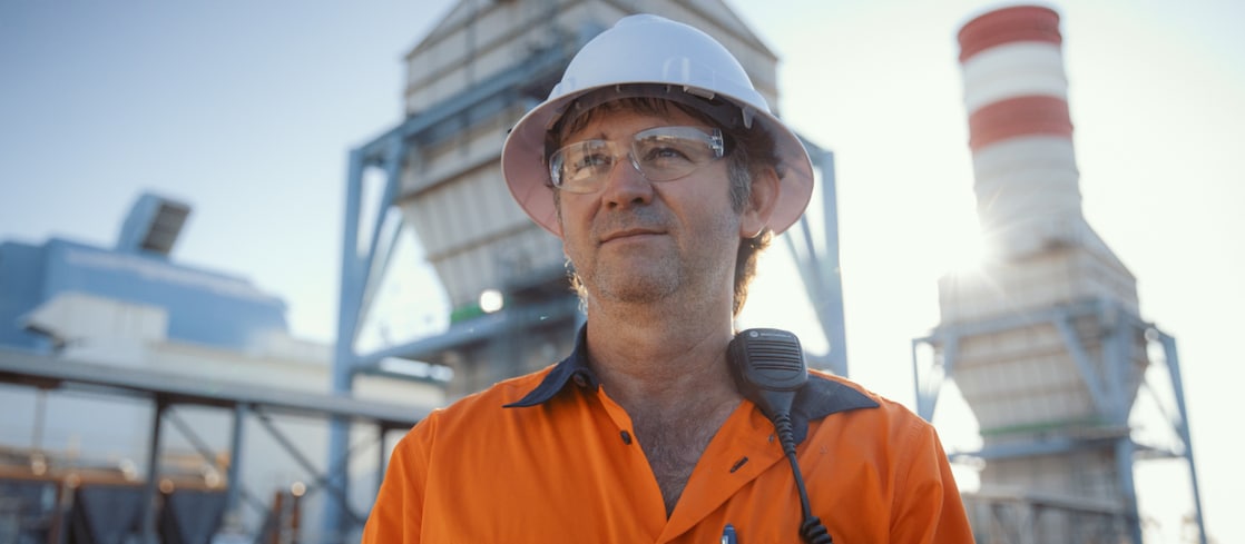 Worker in personal protective gear in front of industrial building.