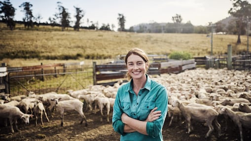 A farmer standing in a grassland and a flock of sheep in regional Australia.