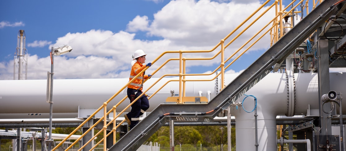 A Shell worker walks up the stairs at an industrial facility in Queensland with a blue sky in the background.