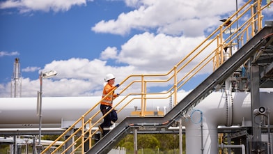 A Shell worker walks up the stairs at an industrial facility in Queensland with a blue sky in the background.