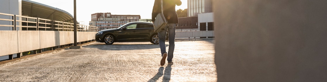 Mature man walking on parking level to his car, talking at the phone