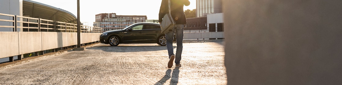Mature man walking on parking level to his car, talking at the phone