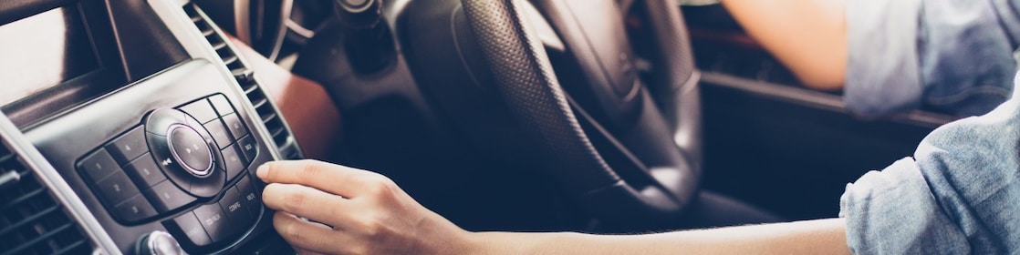 A woman presses a button on a car entertainment system while driving.