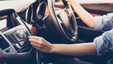 A woman presses a button on a car entertainment system while driving.