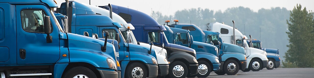 Profiles of different big rigs semi trucks standing in row on parking lot Profiles of different big rig long haul semi trucks with high cab standing on parking lot waiting for loading and possibility of continuing to the destination according to approved schedule