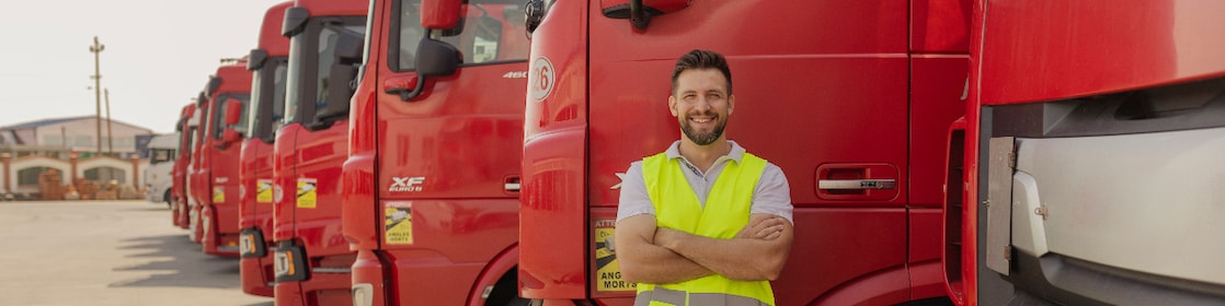 A man stands confidently in front of a lineup of red trucks, showcasing their vibrant color and sturdy design.