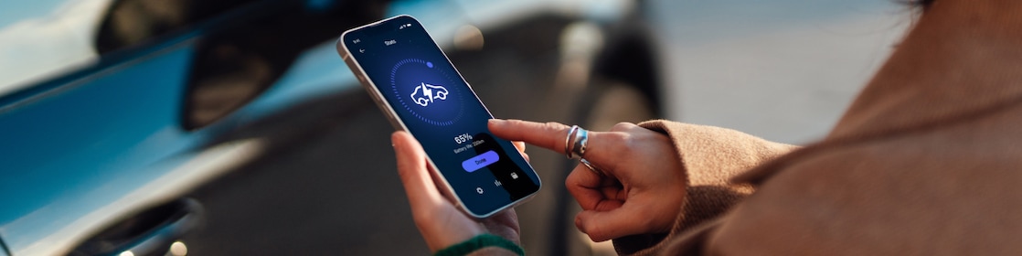Over the shoulder view of young woman using smartphone against an electric car.