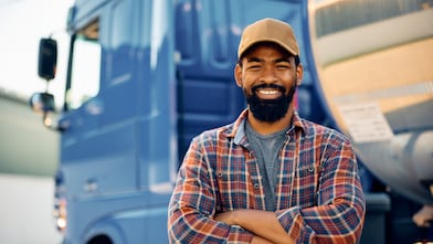 Happy African American truck driver with crossed arms looking at camera.