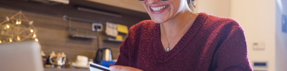 Woman sitting at table, holding card in front of a laptop
