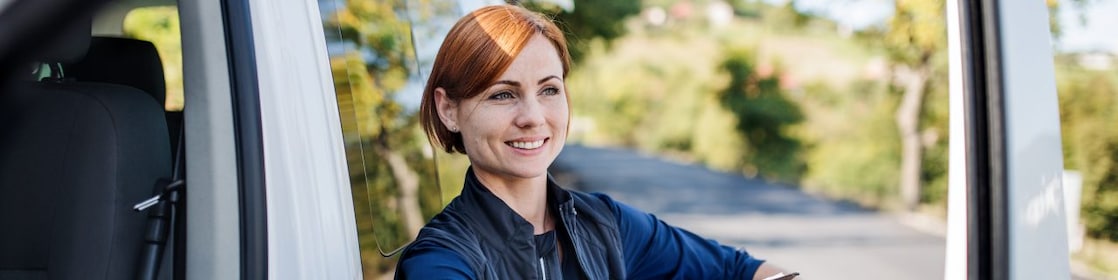 A courier smiles as she unloads parcels from a delivery van.