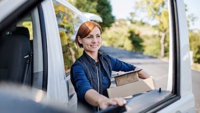 A courier smiles as she unloads parcels from a delivery van.