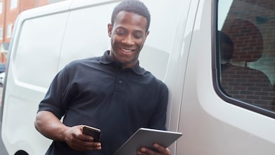 Man on his phone and tablet outside his van