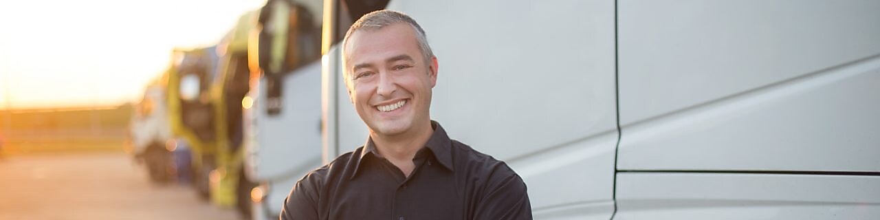 A man stands arms-crossed and smiling in front of multiple parked trucks.