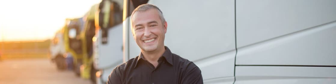 A man stands arms-crossed and smiling in front of multiple parked trucks.
