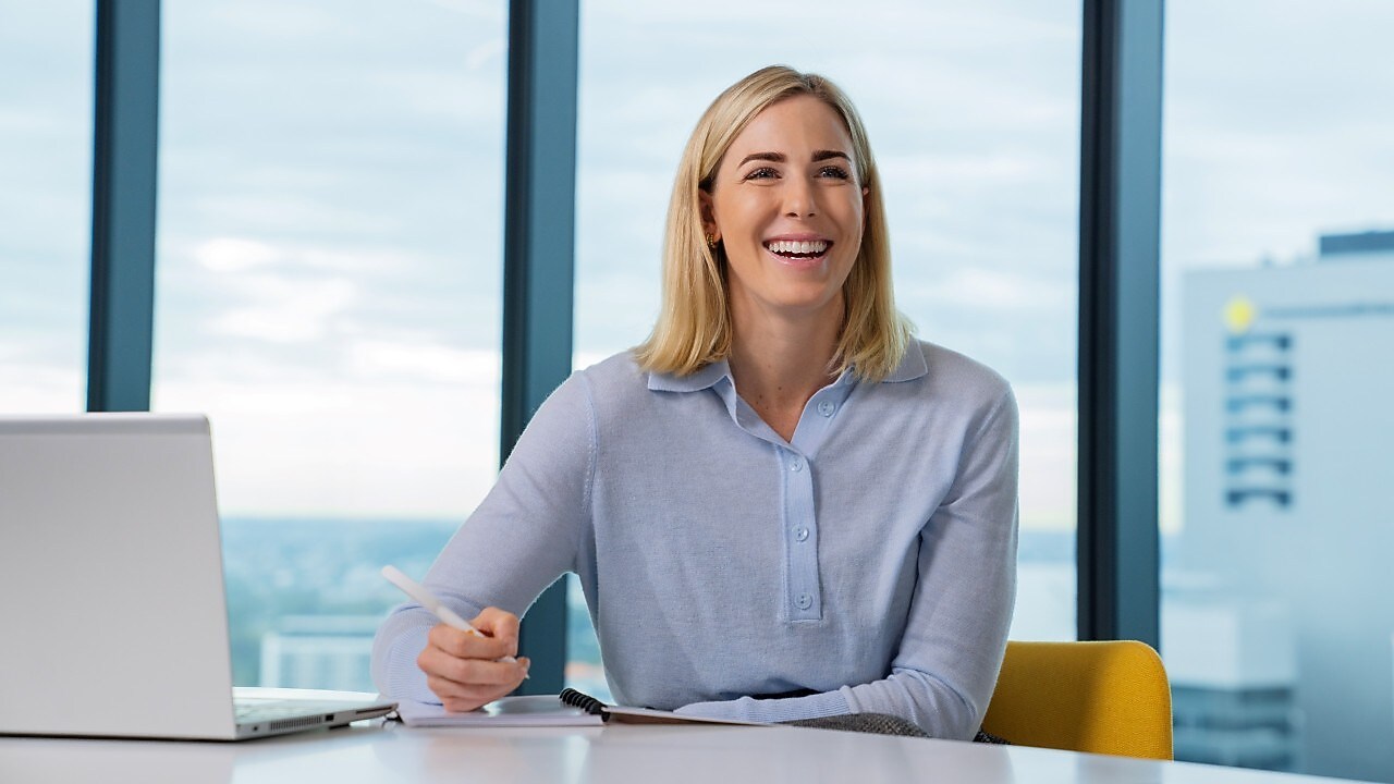 An individual writing in her notebook in front of a laptop
