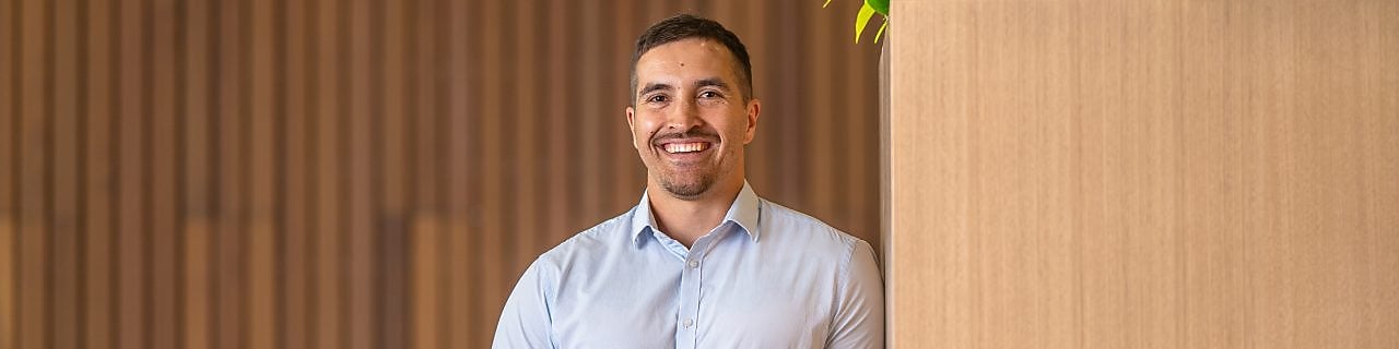 Person in a light blue shirt holds a coffee cup beside a tall wooden planter with green plants in a modern lounge.