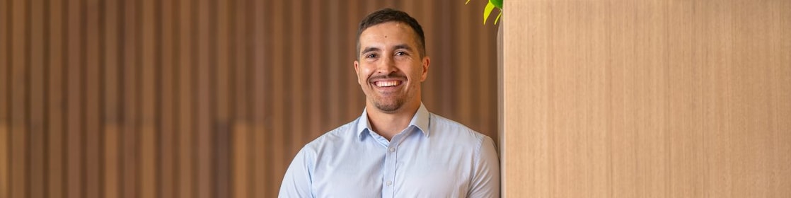 Person in a light blue shirt holds a coffee cup beside a tall wooden planter with green plants in a modern lounge.