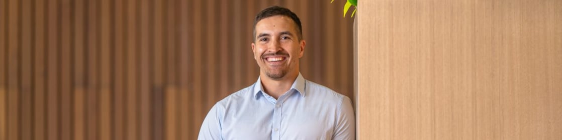 Person in a light blue shirt holds a coffee cup beside a tall wooden planter with green plants in a modern lounge.