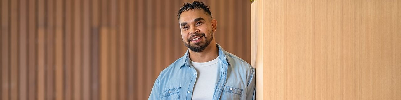Person in a denim shirt holds a coffee and orange power tool beside a wooden planter in a modern lounge.