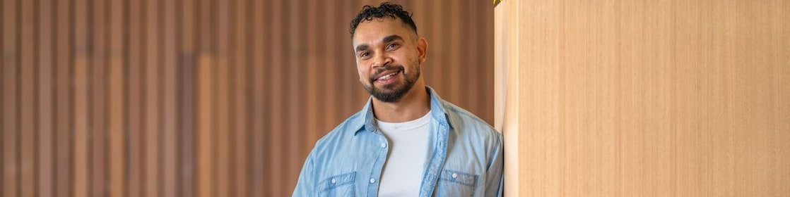 Person in a denim shirt holds a coffee and orange power tool beside a wooden planter in a modern lounge.