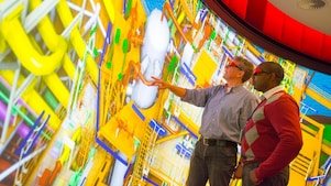 Two men use 3D glasses to look at a large colourful screen