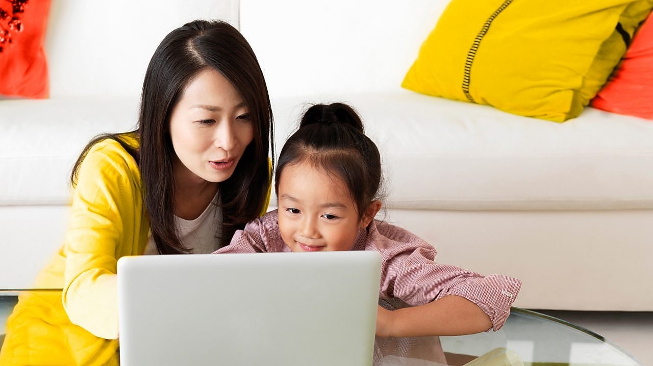 Older woman sitting with child at coffee table, looking at a tablet.
