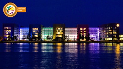 A set of lit office buildings reflect off the water at night