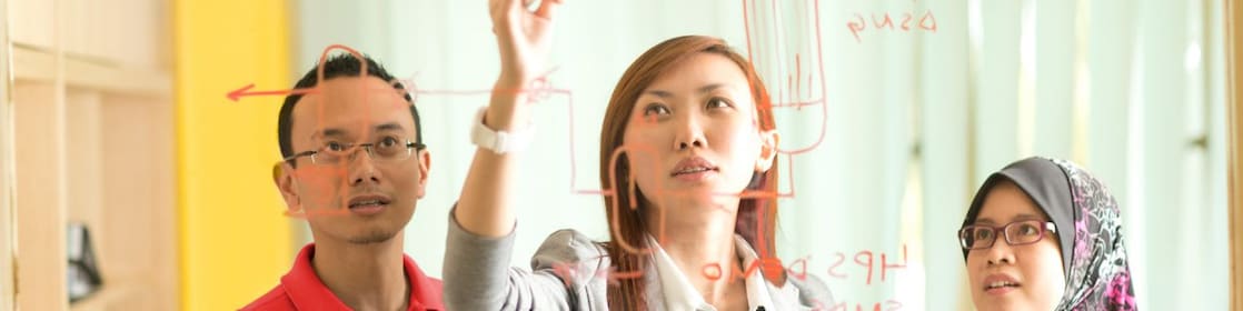 Colleagues gathered standing and discussing metrics on a glass board
