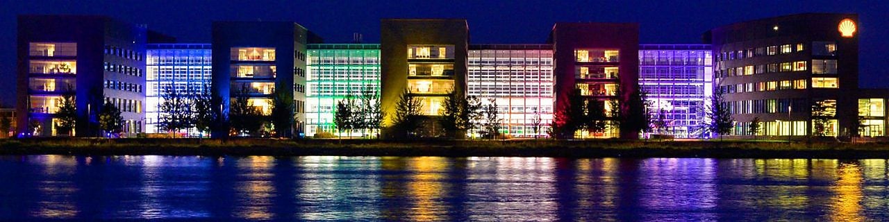 A set of lit office buildings reflect off the water at night