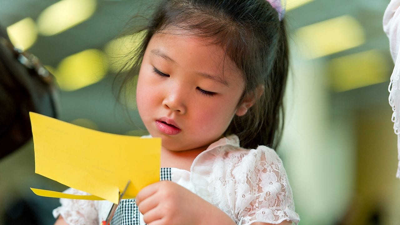 Young girl cutting paper with scissors.