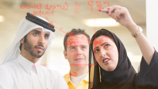 Diverse employees standing discussing while one is writing on the glass board.