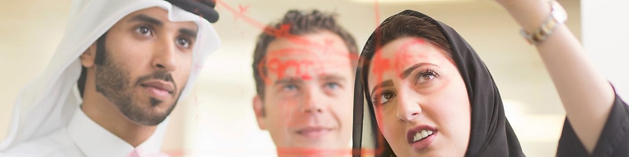 Diverse employees standing discussing while one is writing on the glass board