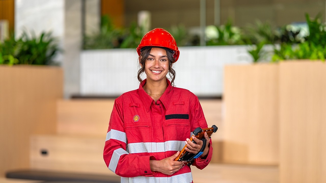 Person in red protective coveralls and hard hat holds tools in a modern indoor space with plants.
