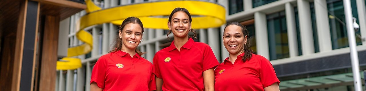 Three team members in red polos stand outside a modern office, yellow ribbon sculpture in the background.