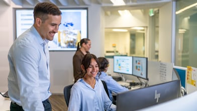 Team collaborates at HP workstations in a modern office; one colleague assists another at a computer.