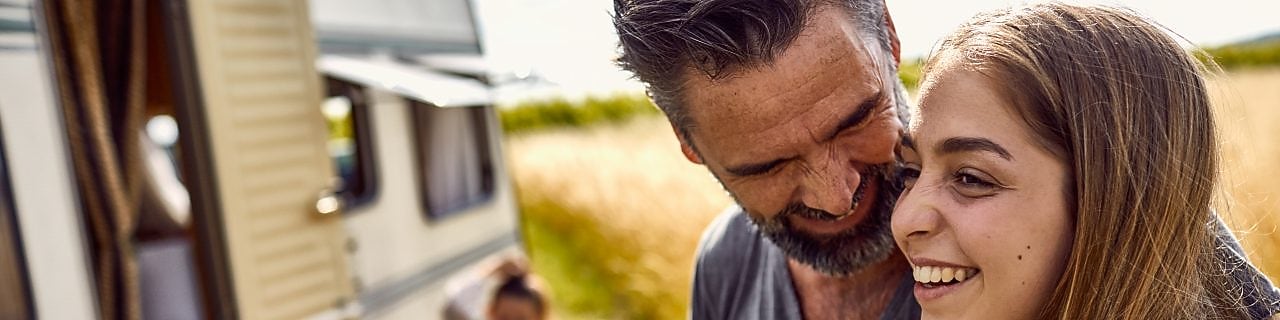 Happy father and daughter on a field next to a caravan