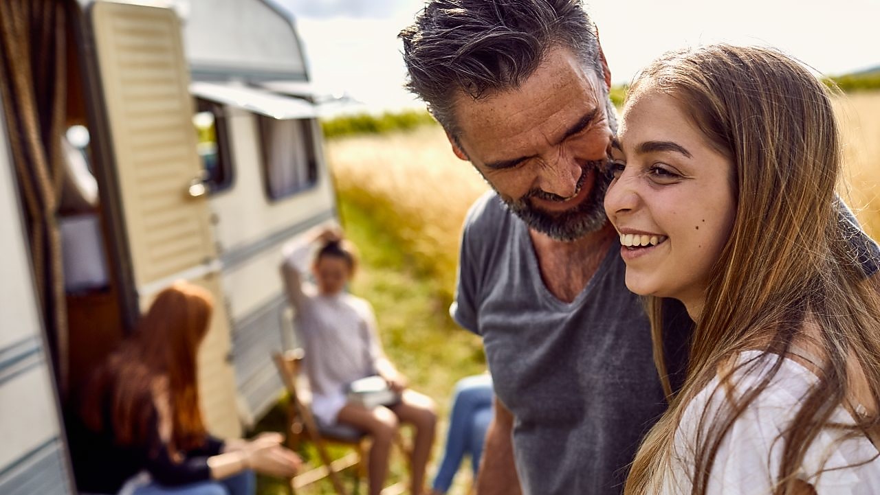 Happy father and daughter on a field next to a caravan