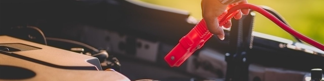 A woman connects red jumper leads to a car battery