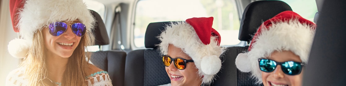 Three children in a car, wearing Santa hats and sunglasses, enjoying a festive ride together.