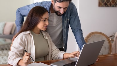 Woman sitting at desk looking at laptop with man looking over her shoulder