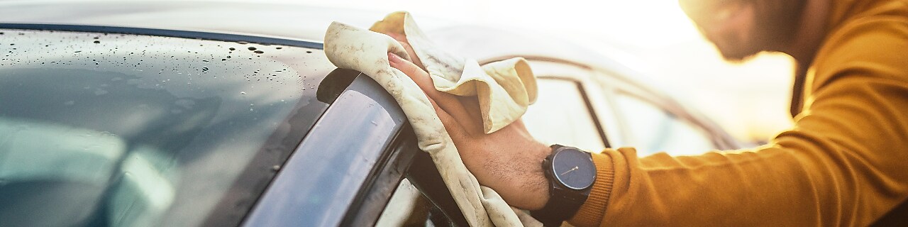 Shot of a happy young man cleaning his car with microfiber cloth on a sunny day.
